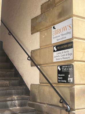 Eine Treppe mit Handläufen und Schildern für Brow's Eyebrow Threading Specialists, The Leather Shop und Chester Clock Tailors.