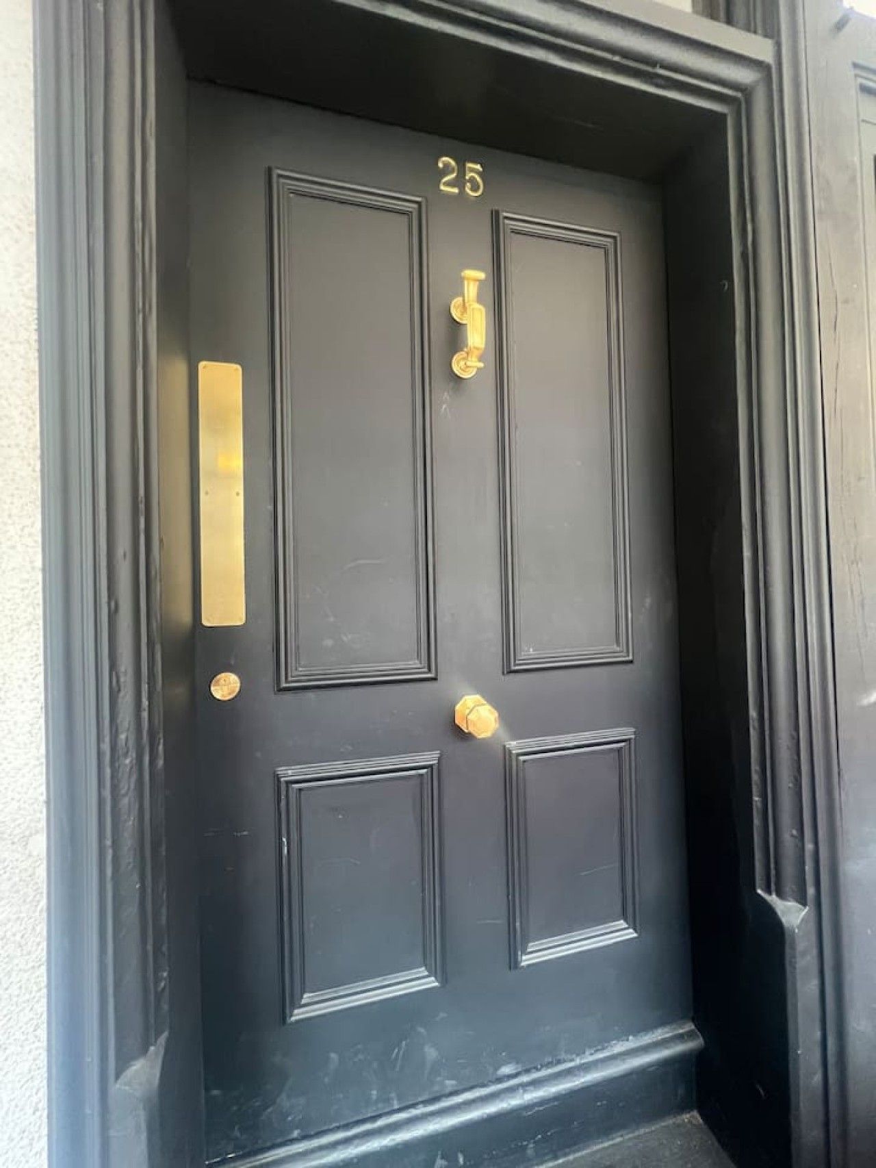 A black door with the number 25, a brass knocker, and a brass mail slot.