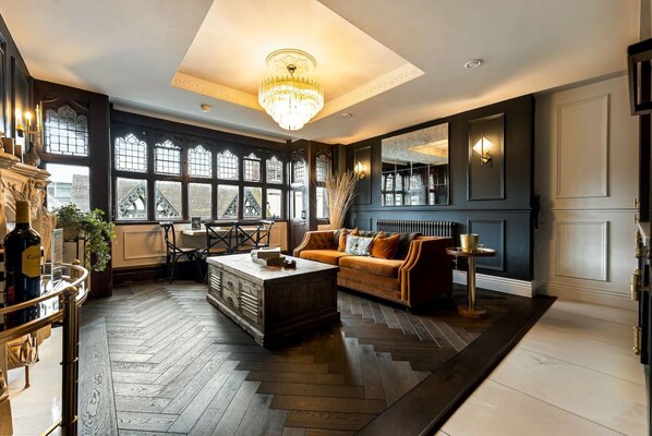 A spacious room with a large chandelier, a sofa, and a coffee table. There are windows with decorative glass panes and a view outside. - Stunning City Centre Apt (Cheshire West and Chester)