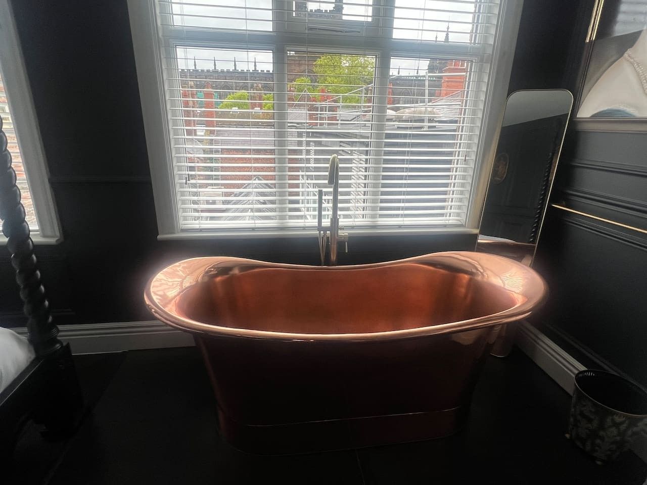 A bathroom with a freestanding bathtub, a window with blinds, and a radiator.
