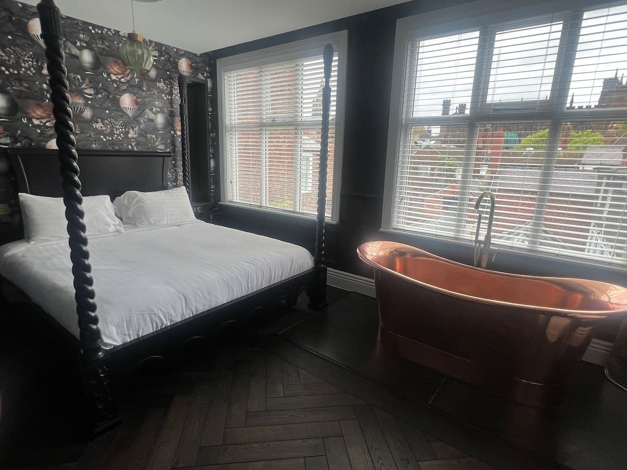 Un dormitorio con cama con dosel, un ventanal con persianas y una bañera independiente.