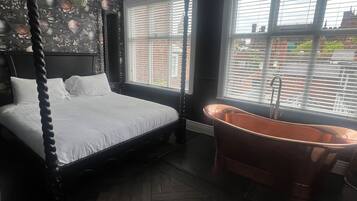 Un dormitorio con cama con dosel, un ventanal con persianas y una bañera independiente.