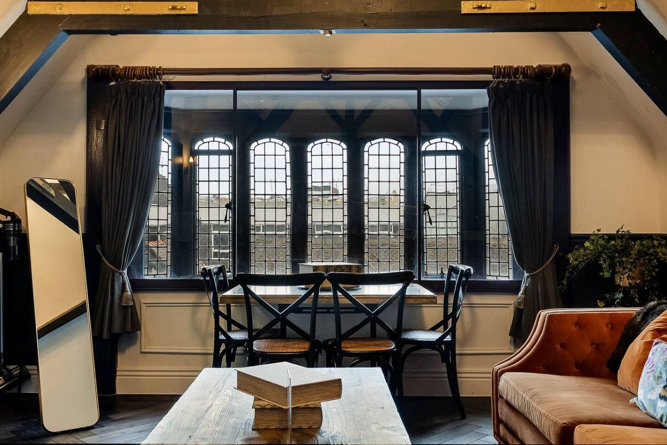 A room with a table, chairs, a sofa, and a large window with multiple panes.