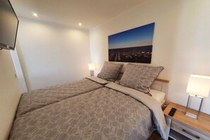 Quarto de hotel com uma cama grande, mesa de cabeceira com abajur e um quadro na parede.