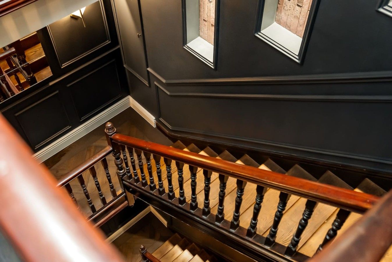 Un escalier avec des balustrades en bois et un mur sombre agrémenté d’une fenêtre.