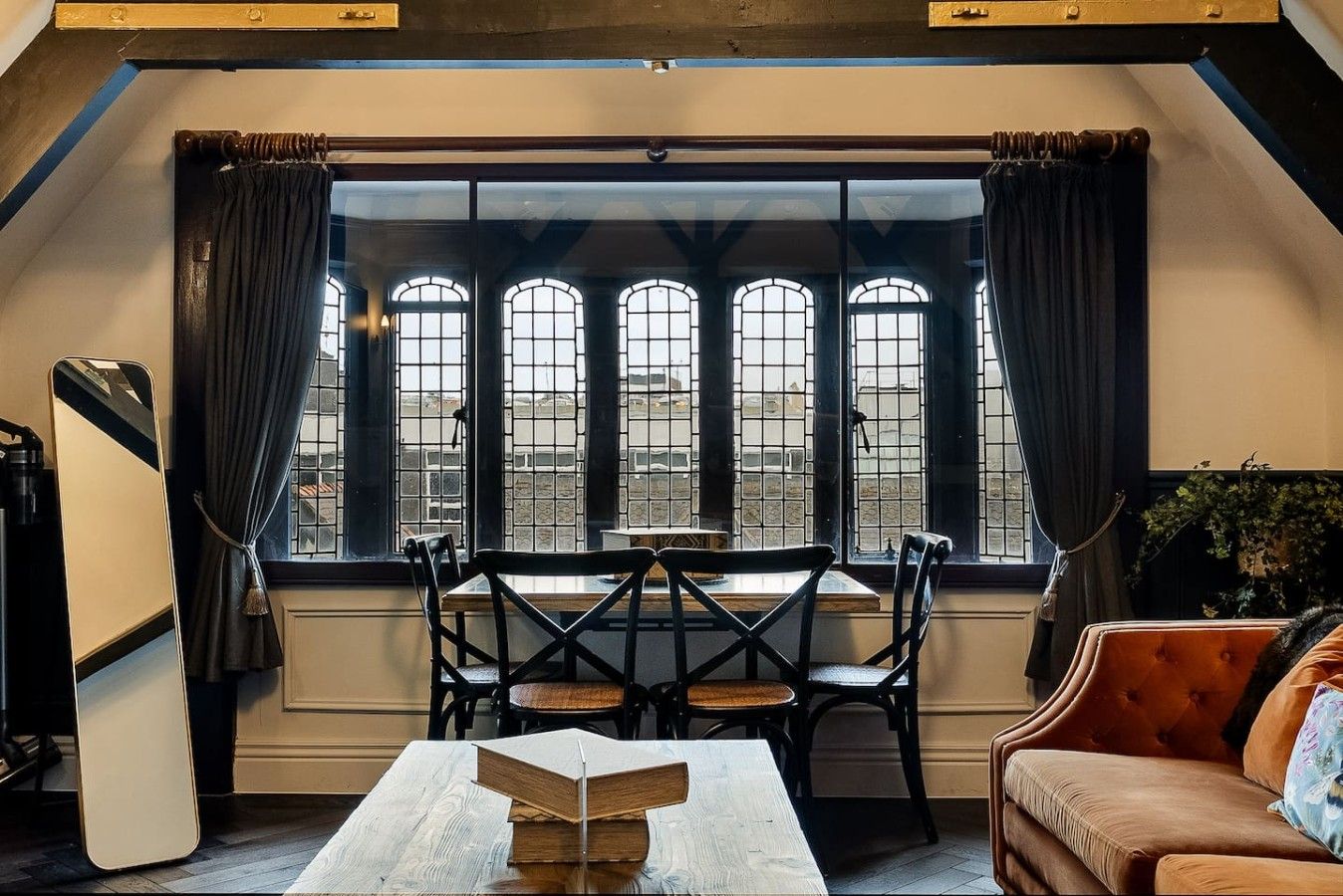 Ein gemütliches Zimmer mit Tisch, Stühlen, einer Couch und einem großen Fenster mit Vorhängen.