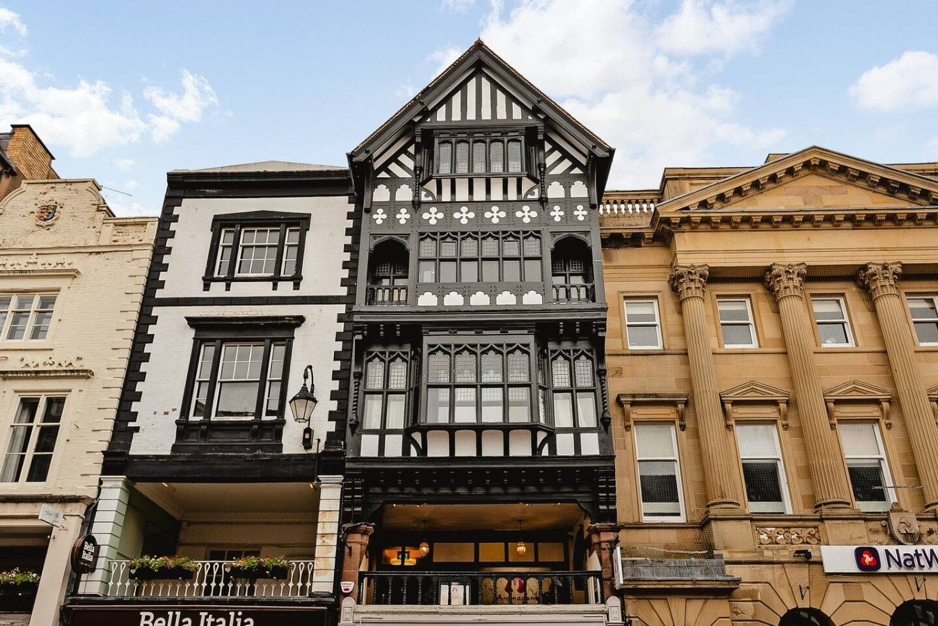 Eine Reihe von Gebäuden mit unterschiedlichen Architekturstilen, darunter ein Haus im Tudorstil mit einer schwarz-weißen Fassade und ein klassizistisches Gebäude mit Säulen.