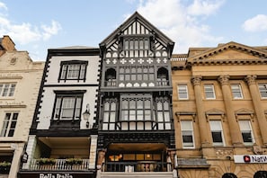 Eine Reihe von Gebäuden mit unterschiedlichen Architekturstilen, darunter ein Haus im Tudorstil mit einer schwarz-weißen Fassade und ein klassizistisches Gebäude mit Säulen.