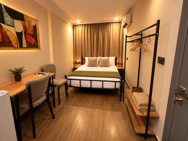 A compact hotel room with a bed, bedside table, chair, and a desk with a plant. - Köşk Butik Otel (Antalya)