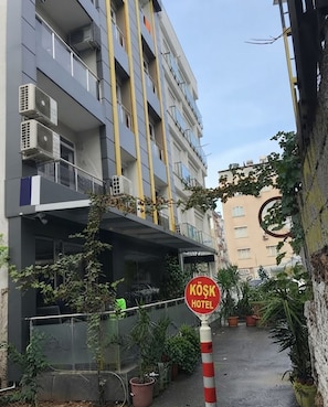 Entrada de un hotel con un letrero que dice 'KÖSK HOTEL' y un área de estar al aire libre cubierta con plantas en macetas.