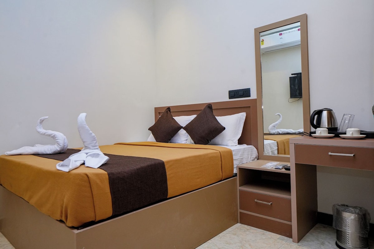 Quarto de hotel com uma cama, uma escrivaninha, um espelho e um cesto de lixo.