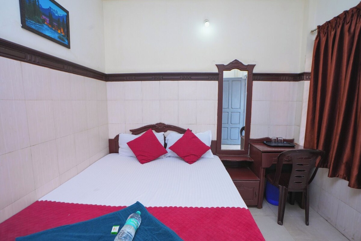 A hotel room with a bed, a desk, a chair, a mirror, and a window with curtains.