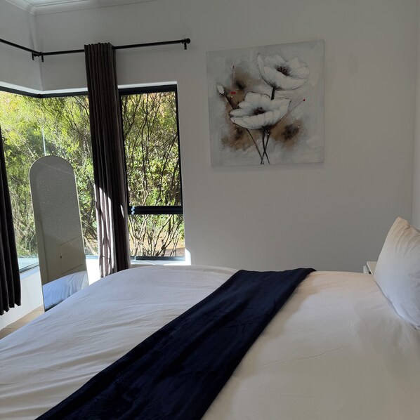 A bedroom with a bed, a window with curtains, and a wall-mounted artwork.