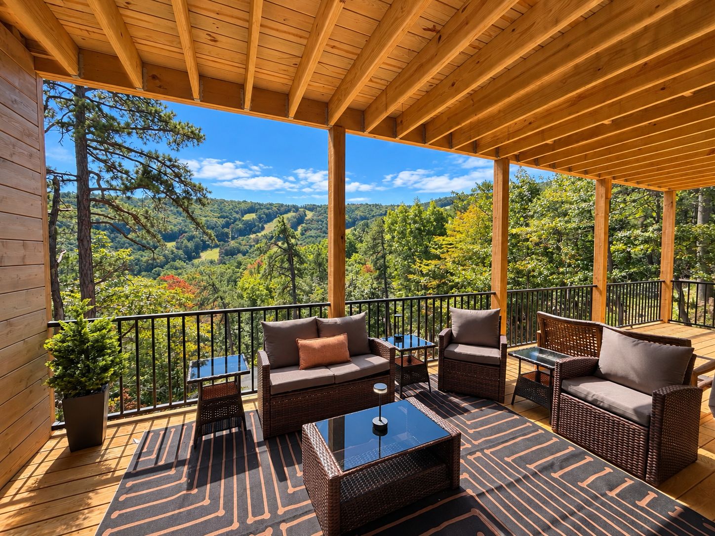 A wooden deck with outdoor furniture, a view of a forested valley, and a clear sky.