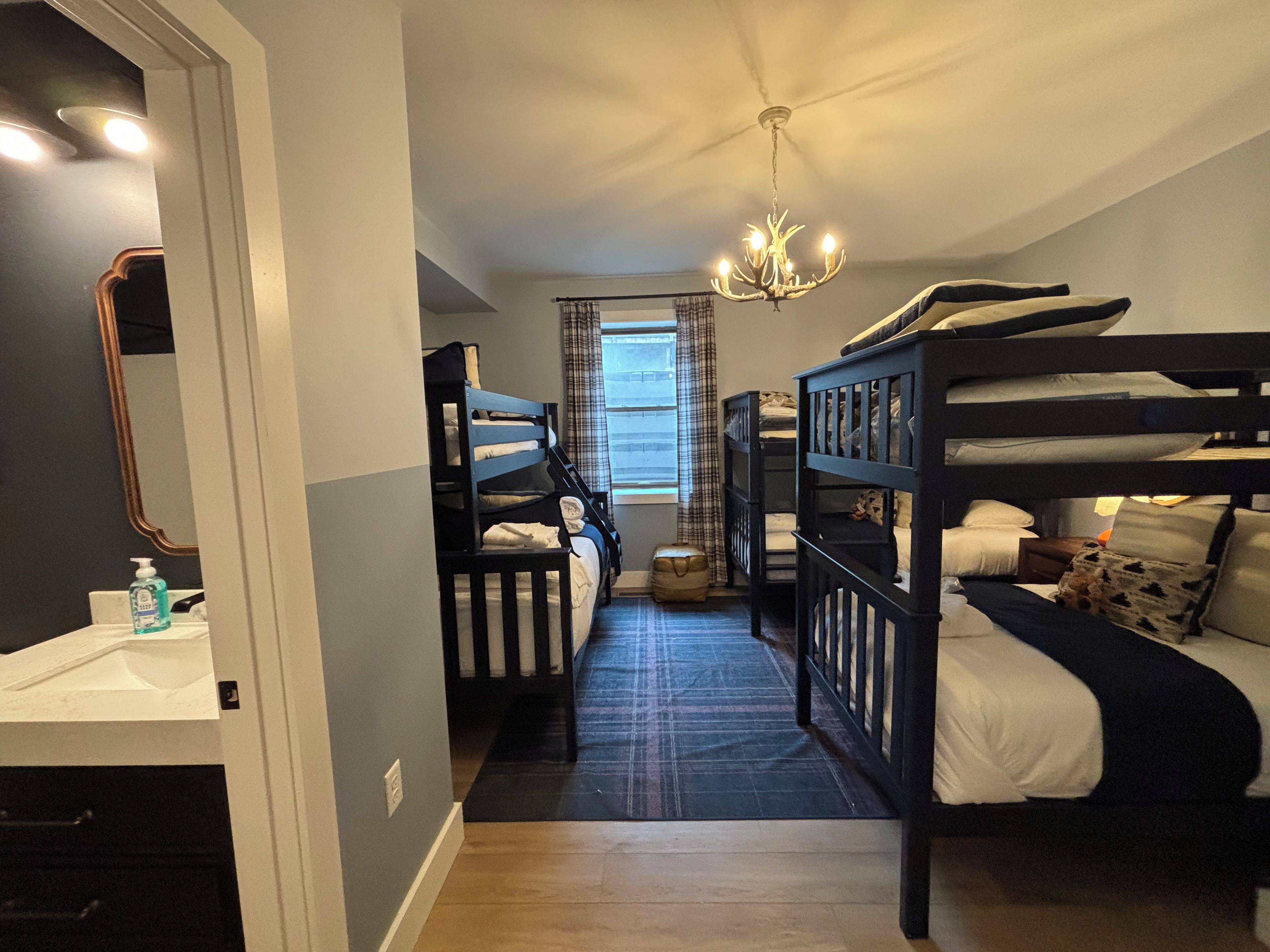 A room with bunk beds, a chandelier, a window with curtains, and a mirror.