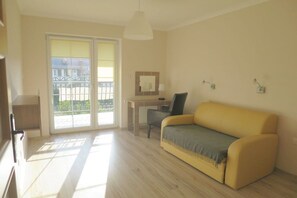 A room with a yellow sofa, a desk with a chair, a large window, and a balcony. - Holiday apartment with 4 bedrooms (Grzybowo)