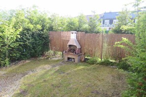 Ein Garten mit einem Steingrill, einem Holzzaun und einem Pflasterweg.