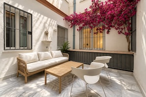 A sunlit patio with a sofa, a wooden table, and chairs, a potted plant, and a window with a view of the sky. - Genteel Home Reyes Catolicos Sevilla (Seville)