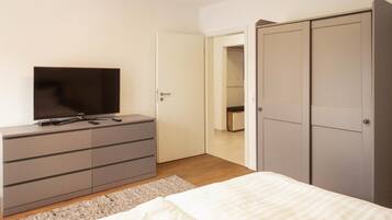 Ein Schlafzimmer mit einem Bett, einem Fernseher auf einer Kommode, einem Kleiderschrank und einer Tür zu einem anderen Raum.