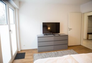 A bedroom with a bed, a grey dresser, a television, and a door. - Apartment 'Haus Salinen 2' with Balcony, Wi-Fi and Air Conditioning (Bad Rothenfelde)