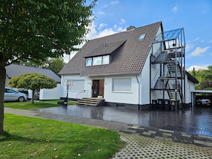 Un edificio residenziale su due piani con tetto spiovente, una scala a vista e un garage.
