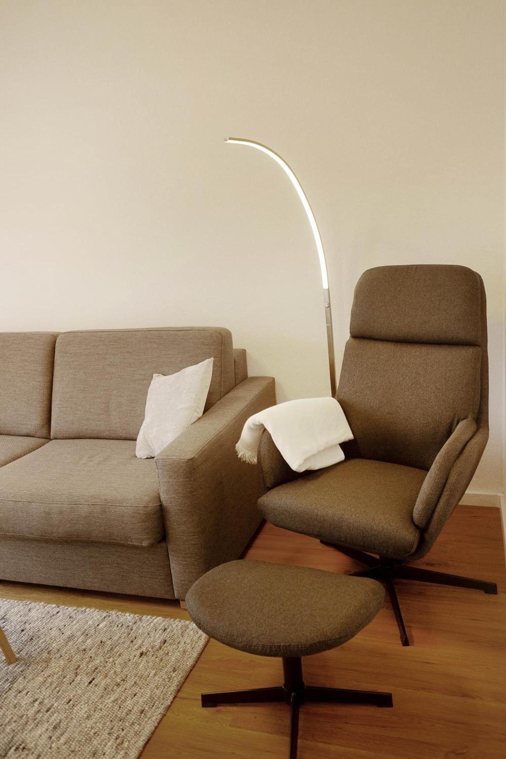 A modern living room with a sofa, a chair, a small ottoman, and a floor lamp.