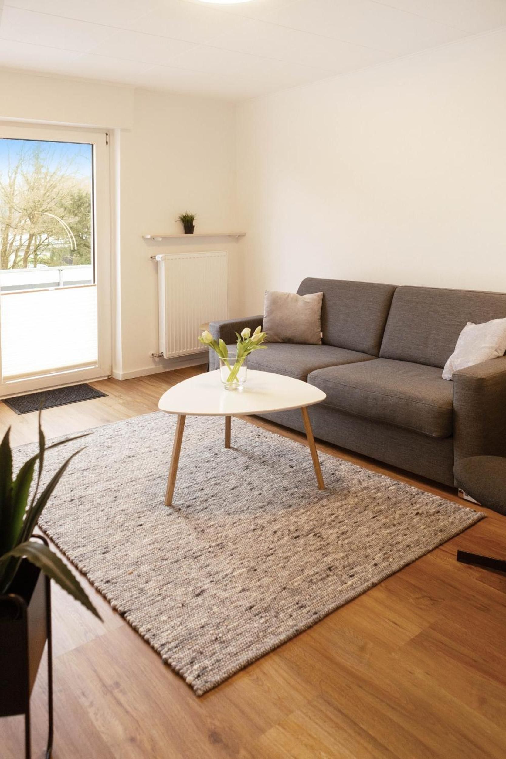 Ein Wohnzimmer mit einem grauen Sofa, einem kleinen weißen Couchtisch und einem grauen Teppich.