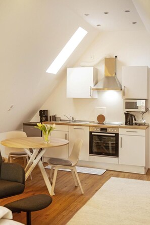 A modern kitchen with white cabinetry, a built-in oven, and a microwave. There is a dining table with chairs and a vase of flowers. - Room 'Haus Salinen Loft 5' with Balcony, Wi-Fi and Air Conditioning (Bad Rothenfelde)