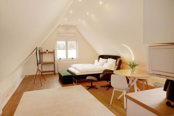 A bedroom with a bed, bedside table, chair, and a desk with a chair. There is a window with a view of trees. - Room 'Haus Salinen Loft 5' with Balcony, Wi-Fi and Air Conditioning (Bad Rothenfelde)
