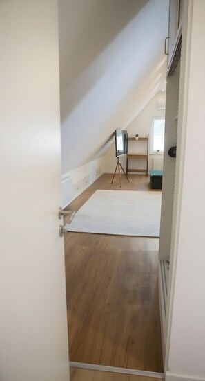 An attic room with a wooden floor, a white wall, and a tripod-mounted camera. - Room 'Haus Salinen Loft 5' with Balcony, Wi-Fi and Air Conditioning (Bad Rothenfelde)