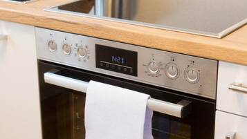 A kitchen with a stainless steel oven, a digital clock displaying 14:21, and a white towel hanging on the oven door.