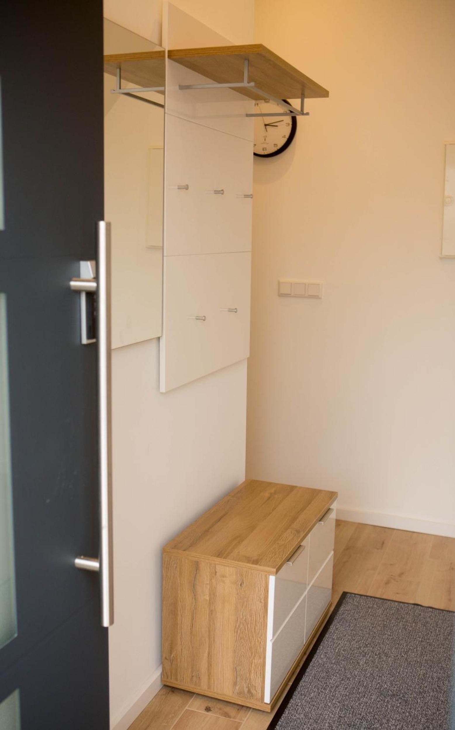 Ein Zimmer mit einem Holzkabinett, einem weißen Wandregal, einer Tür mit Griff und einer Wanduhr.