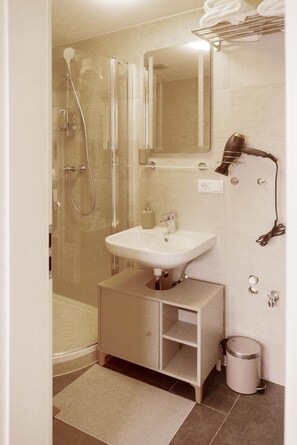 Een moderne badkamer met een glazen douchecabine, een wastafel met spiegel en een haardroger aan de muur.