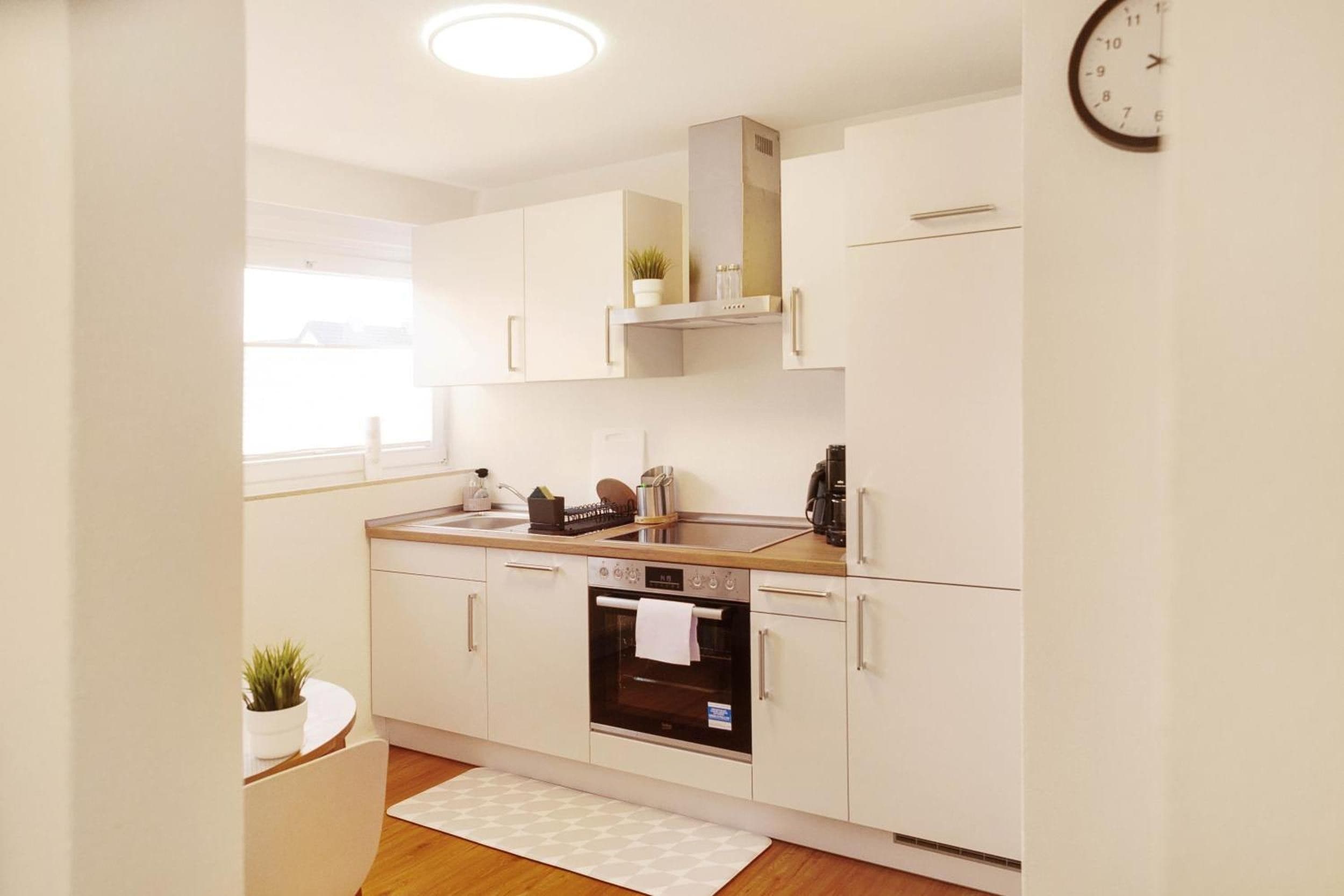 Une cuisine moderne avec des armoires blanches, un four encastré et une horloge au mur.