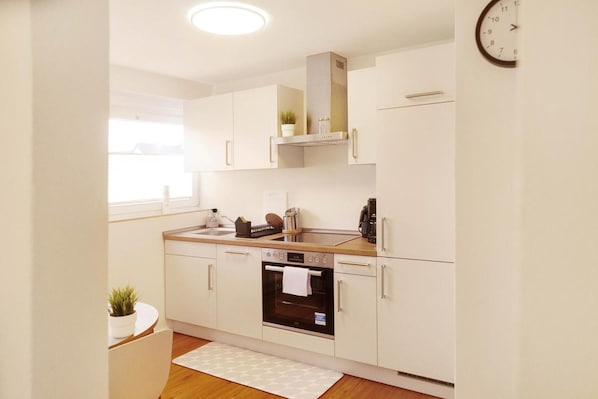 Een moderne keuken met witte kasten, een inbouwoven en een klok aan de muur.