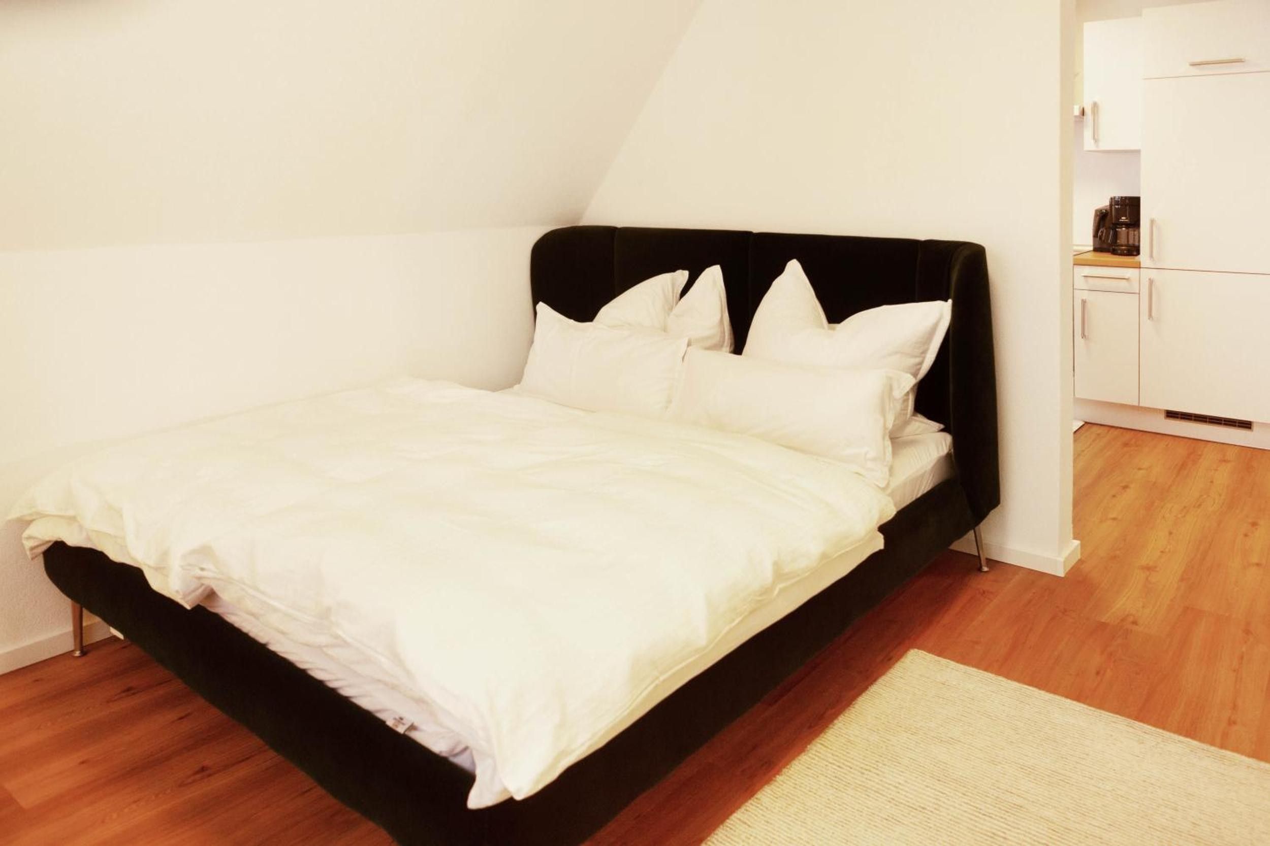 Ein Einzelbett mit schwarzem Kopfteil und weißer Bettwäsche in einem Zimmer mit Holzboden und weißen Wänden.