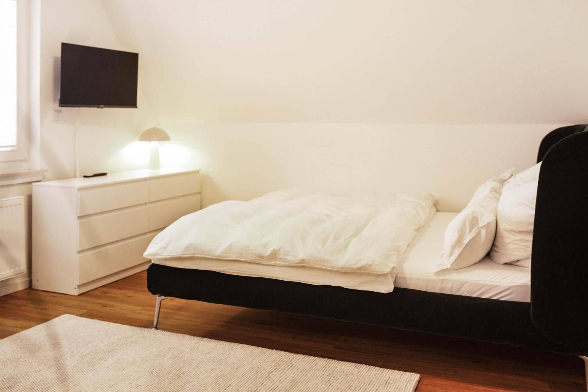 Une chambre à coucher avec un lit, une table de chevet, une lampe et un téléviseur fixé au mur.
