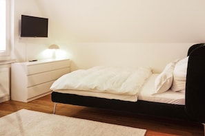 Een slaapkamer met een bed, nachtkastje, lamp en een aan de muur bevestigde televisie.