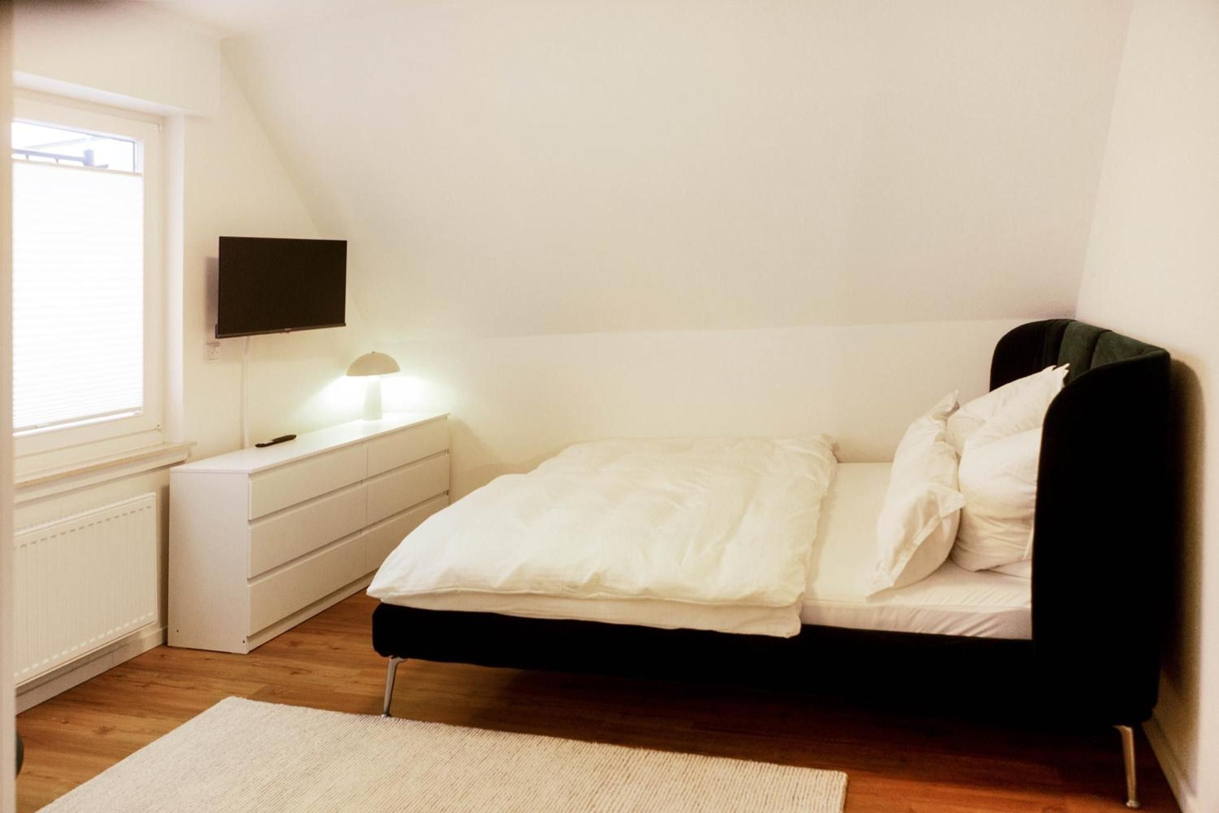 A bedroom with a bed, a nightstand, a lamp, and a TV mounted on the wall.