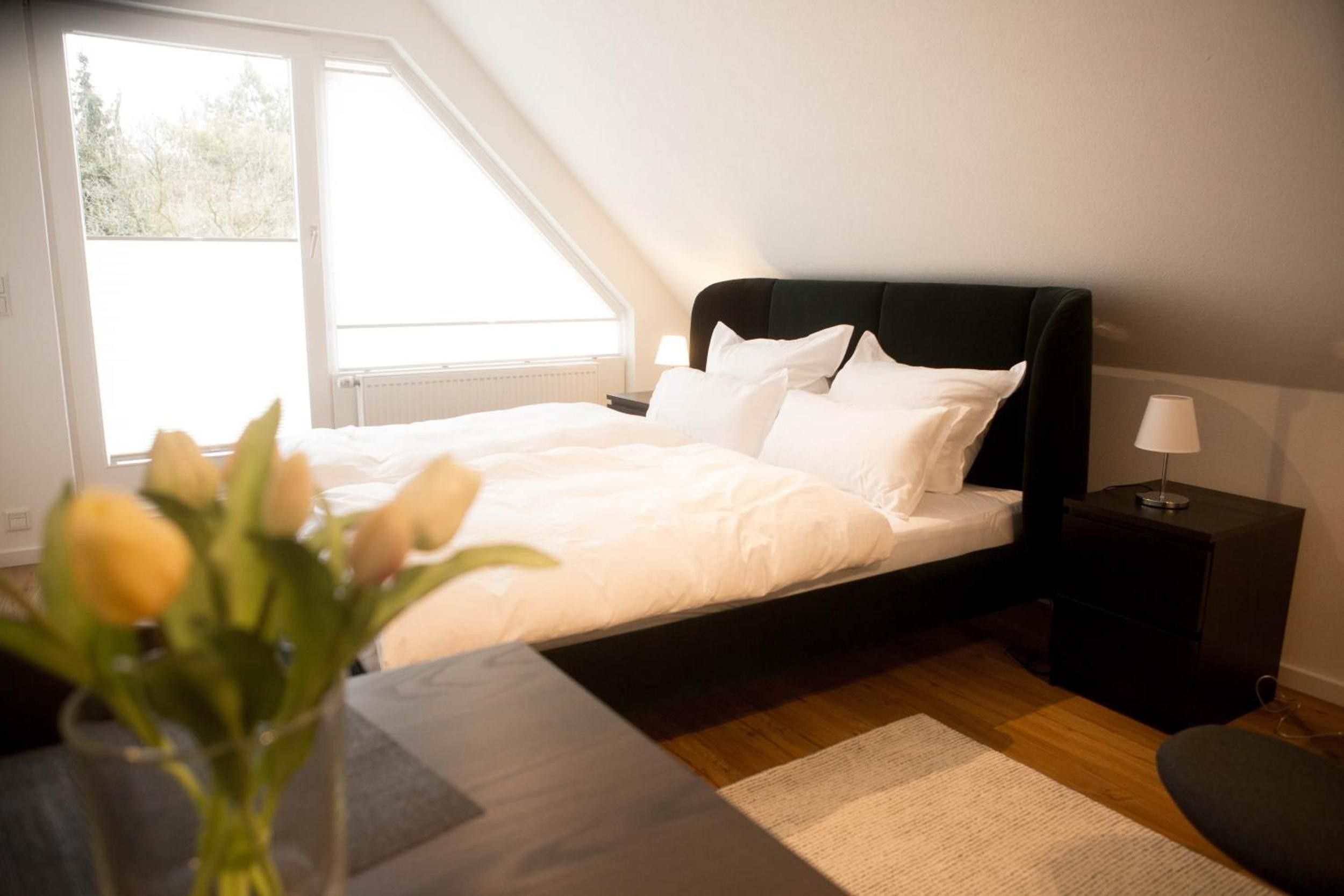 A bedroom with a bed, a nightstand, a lamp, and a view of the outdoors.