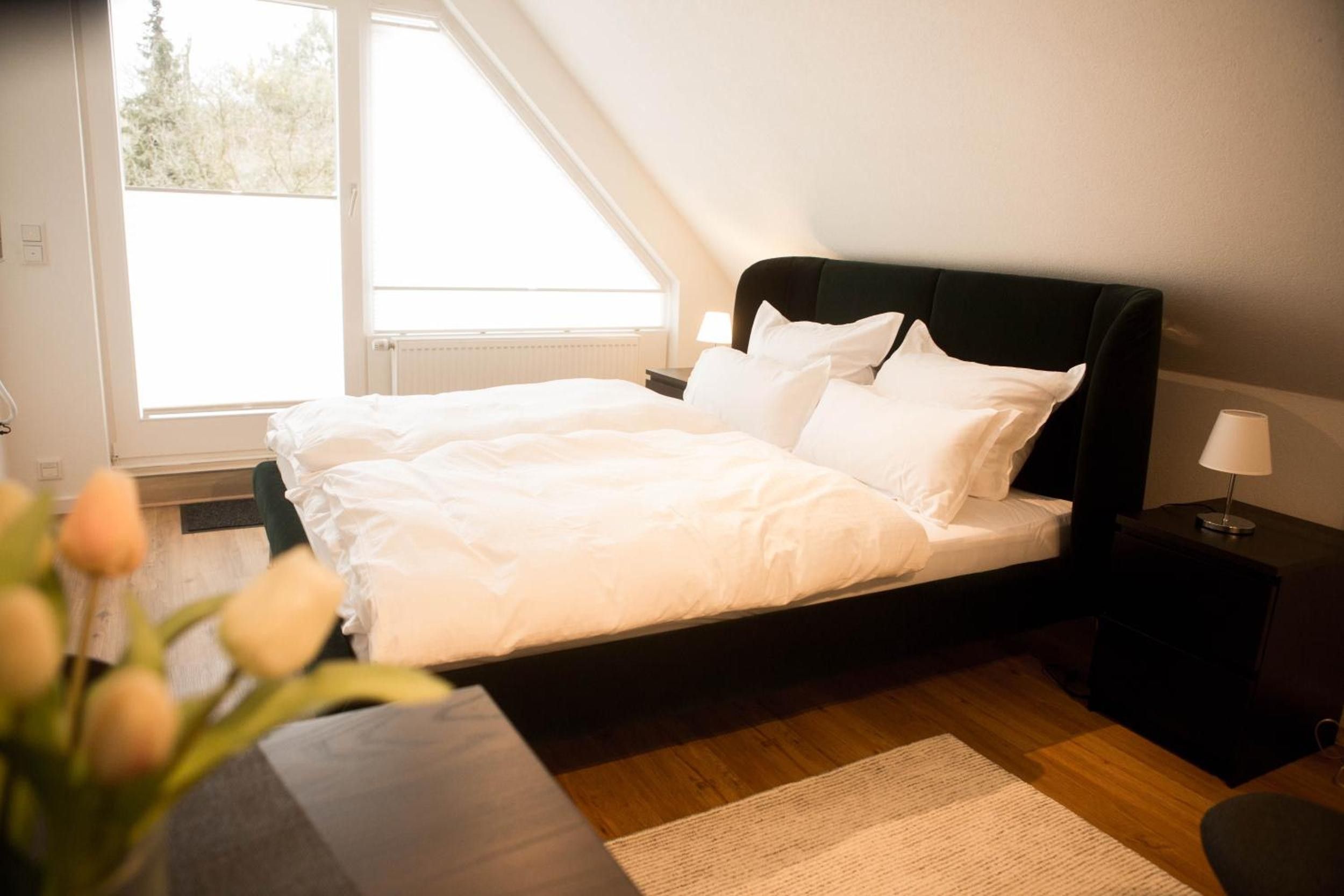 Ein Schlafzimmer mit Bett, Nachttisch, Lampe und Fenster.