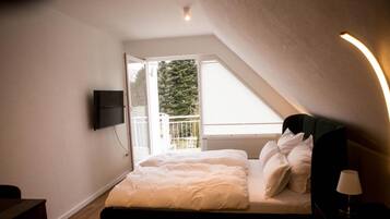 A bedroom with a bed, a TV mounted on the wall, a window with a view of trees, and a lamp on a bedside table.