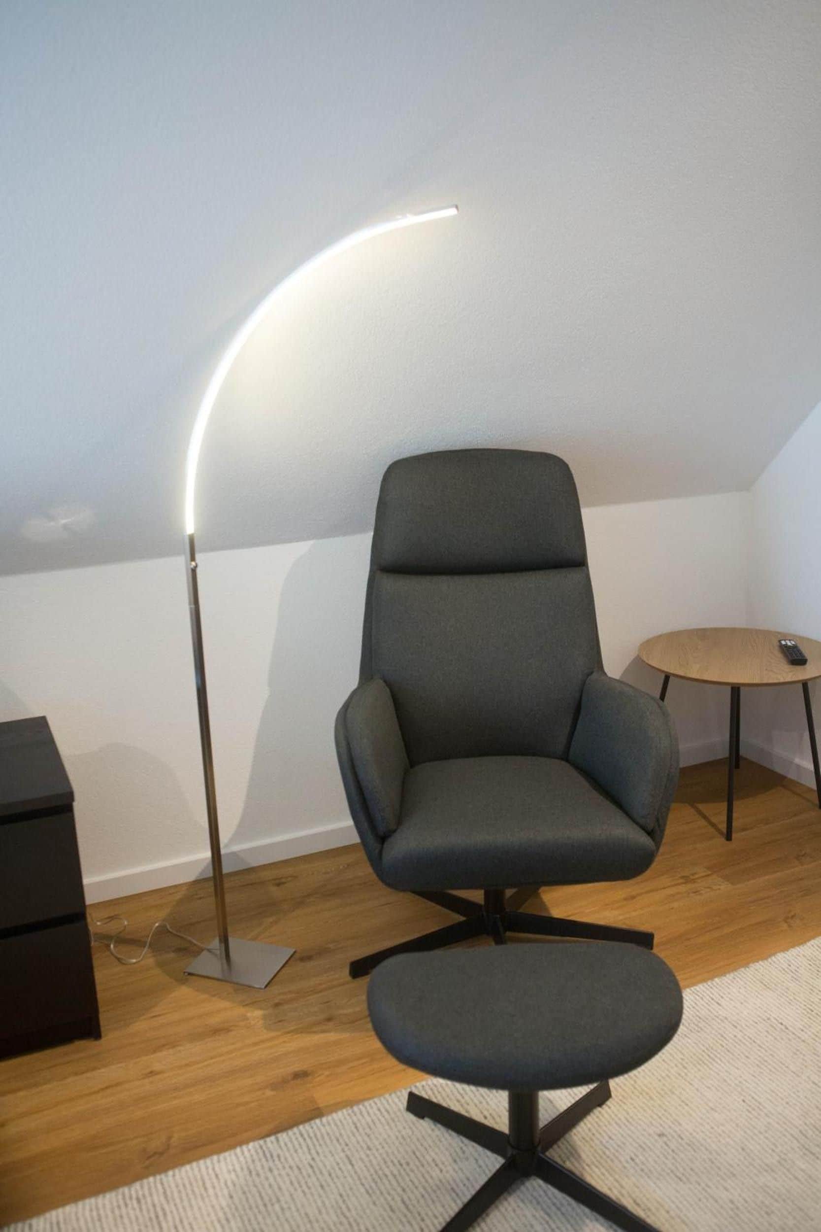Un fauteuil moderne doté d’un haut dossier et accompagné d’un repose-pieds assorti, placés sur un plancher en bois avec un tapis de couleur claire.