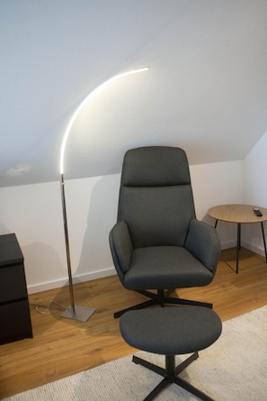 Een moderne stoel met een hoge rugleuning en een bijpassend pouf, staand op een houten vloer met een lichtgekleurd vloerkleed.