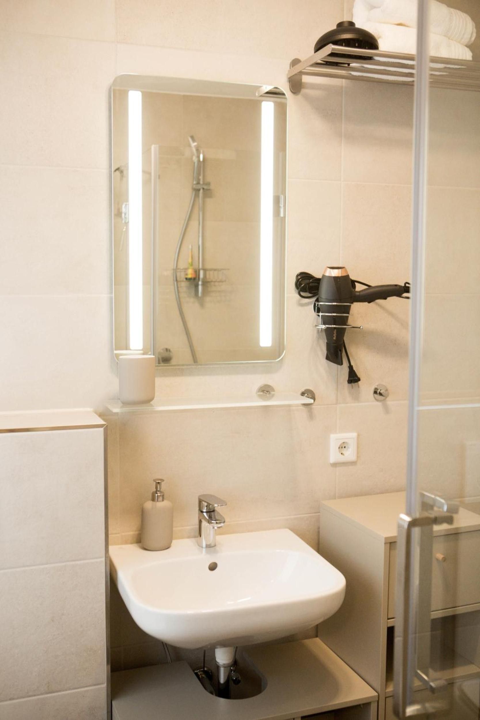 Ein Badezimmer mit einem weißen Waschbecken, einem Spiegel, einem Handtuchhalter und einem an der Wand befestigten Föhn.