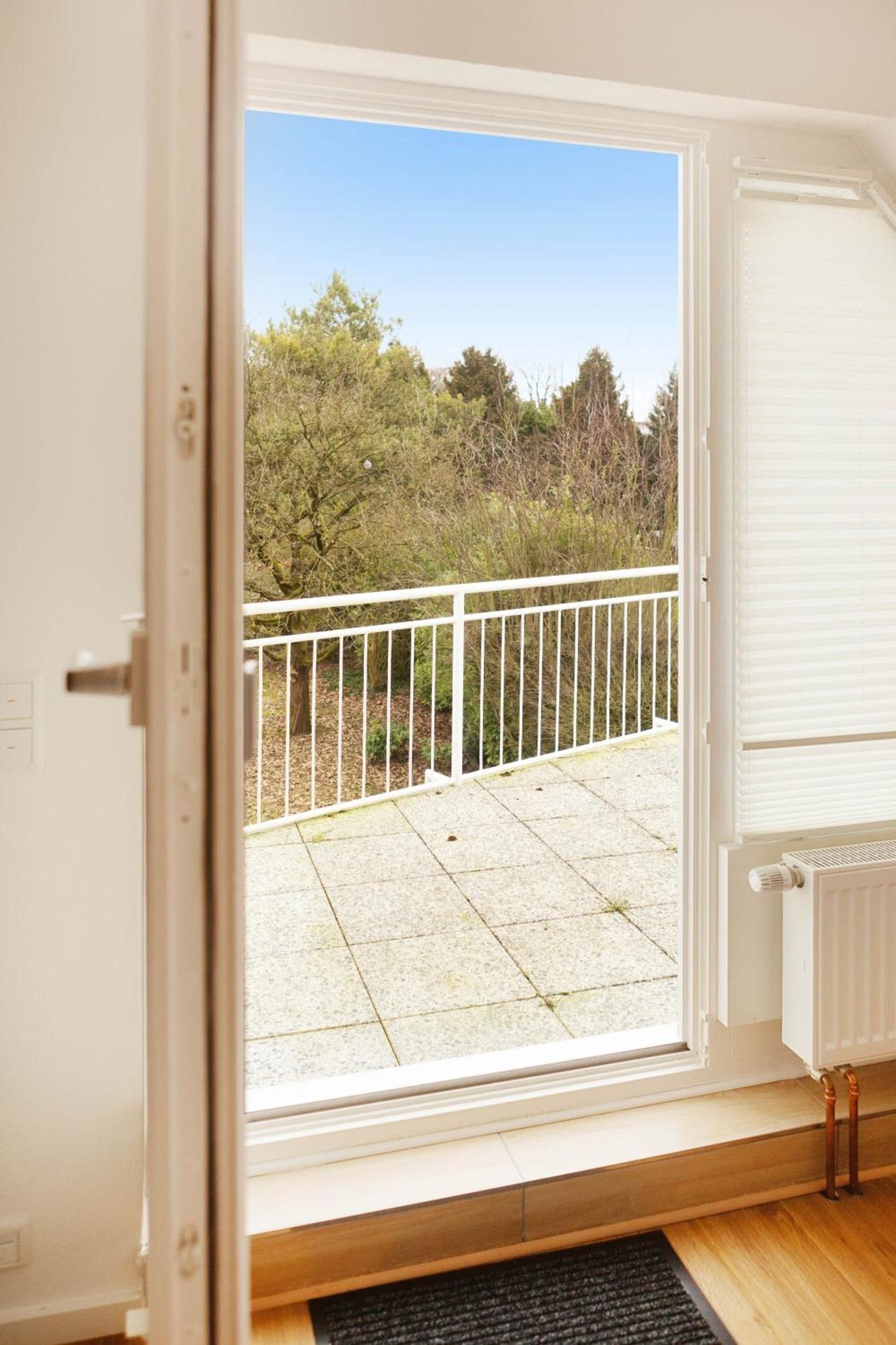 Une pièce dotée d’une porte-fenêtre coulissante qui donne sur un espace extérieur agrémenté d’une rambarde en métal blanc et d’un sol carrelé.