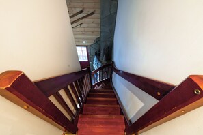 A wooden staircase with a handrail, leading to a room with a stone wall and a window. - Levin Otava - Comfy Apt in Levi Centre (Kittilä)