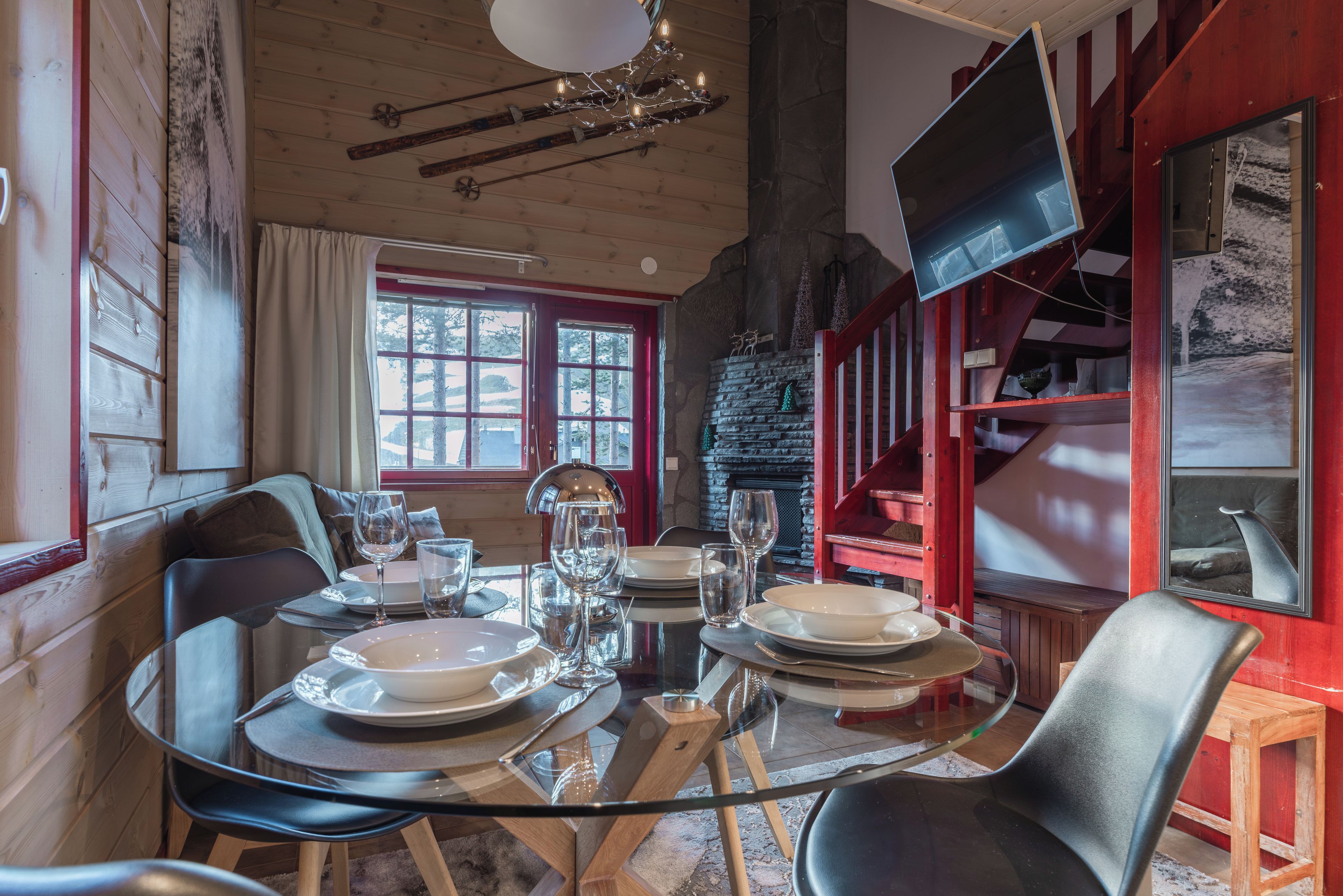 A dining area with a round table set for four, a fireplace, and a television mounted on the wall.