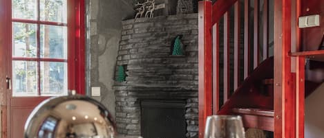 A dining area with a stone fireplace, wooden ceiling, and a red railing.