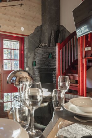 A dining area with a stone fireplace, wooden ceiling, and a red railing. - Levin Otava - Comfy Apt in Levi Centre (Kittilä)